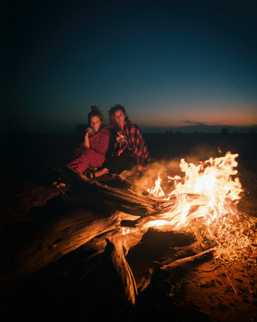 Two travelers warming themselves beside a campfire at night