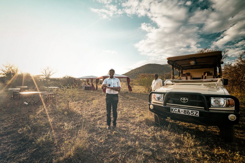 Safari team standing beside an off-road vehicle at sunset