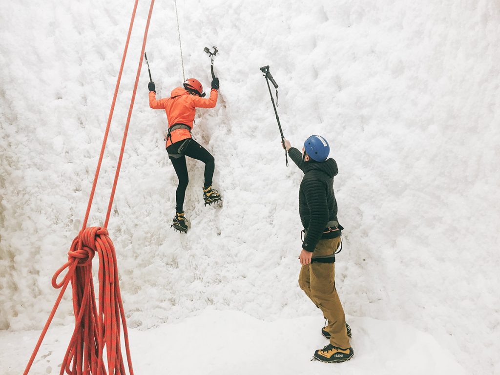 Climber on an indoor ice wall with a belayer below