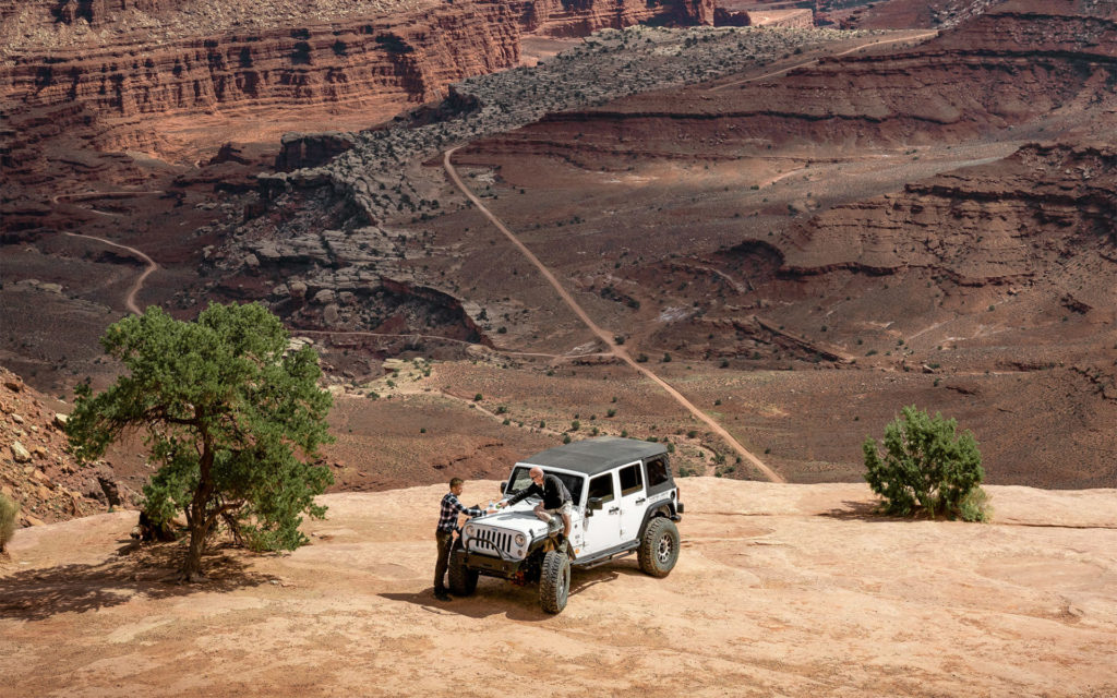 White Jeep on a sandstone overlook above a winding canyon road