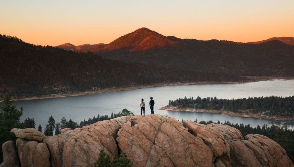 Two hikers on a granite viewpoint above a lake at sunset