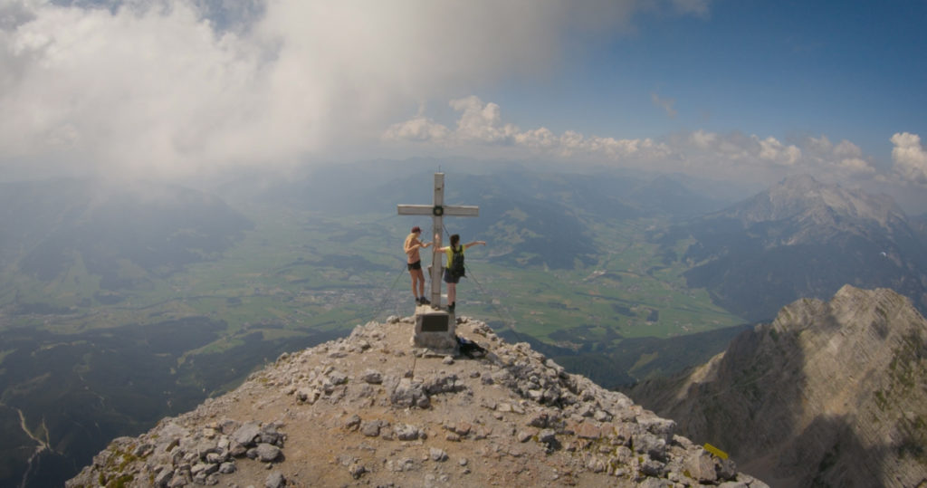 Hikers beside a summit cross above an alpine valley