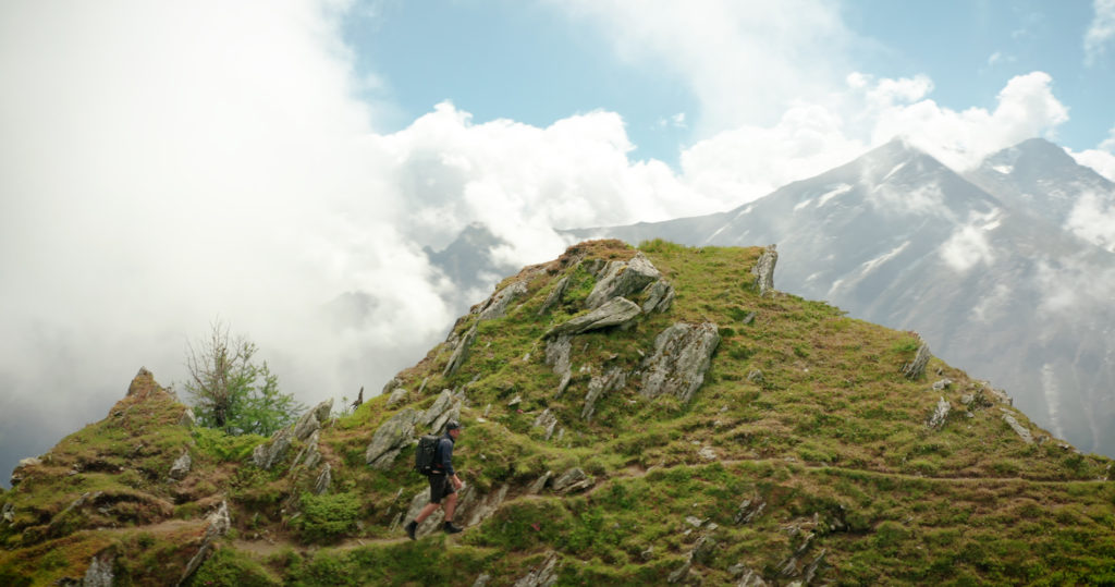 Hiker crossing a grassy ridge beneath jagged alpine peaks