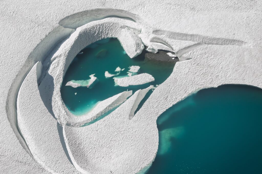 Turquoise meltwater pools across a snow-covered glacier