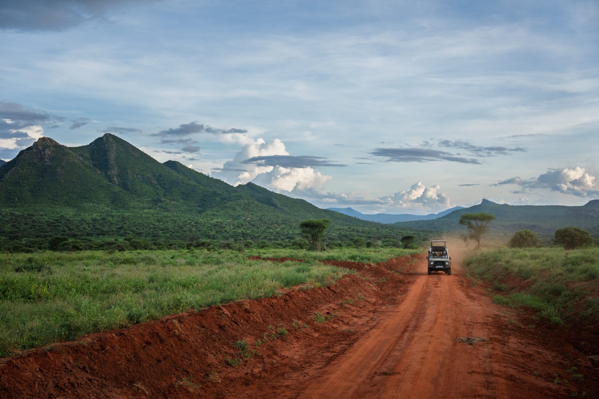 Safari vehicle travelling along a red road toward Kenyan mountains