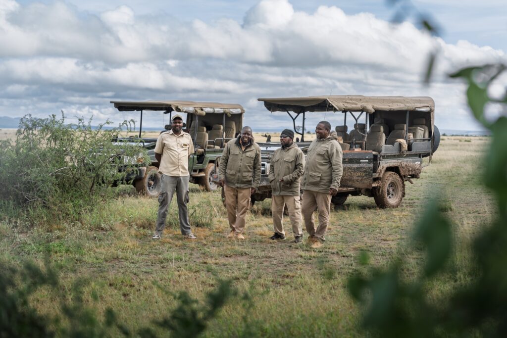 Kenyan safari guides standing beside open game-drive vehicles