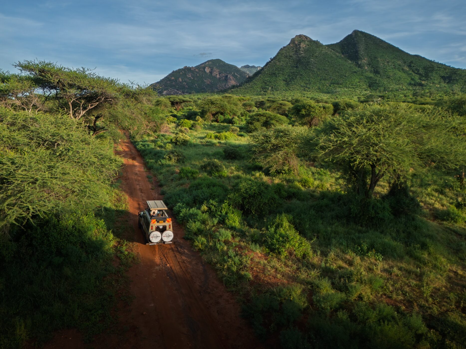 Safari vehicle following a narrow road through lush Kenyan bush