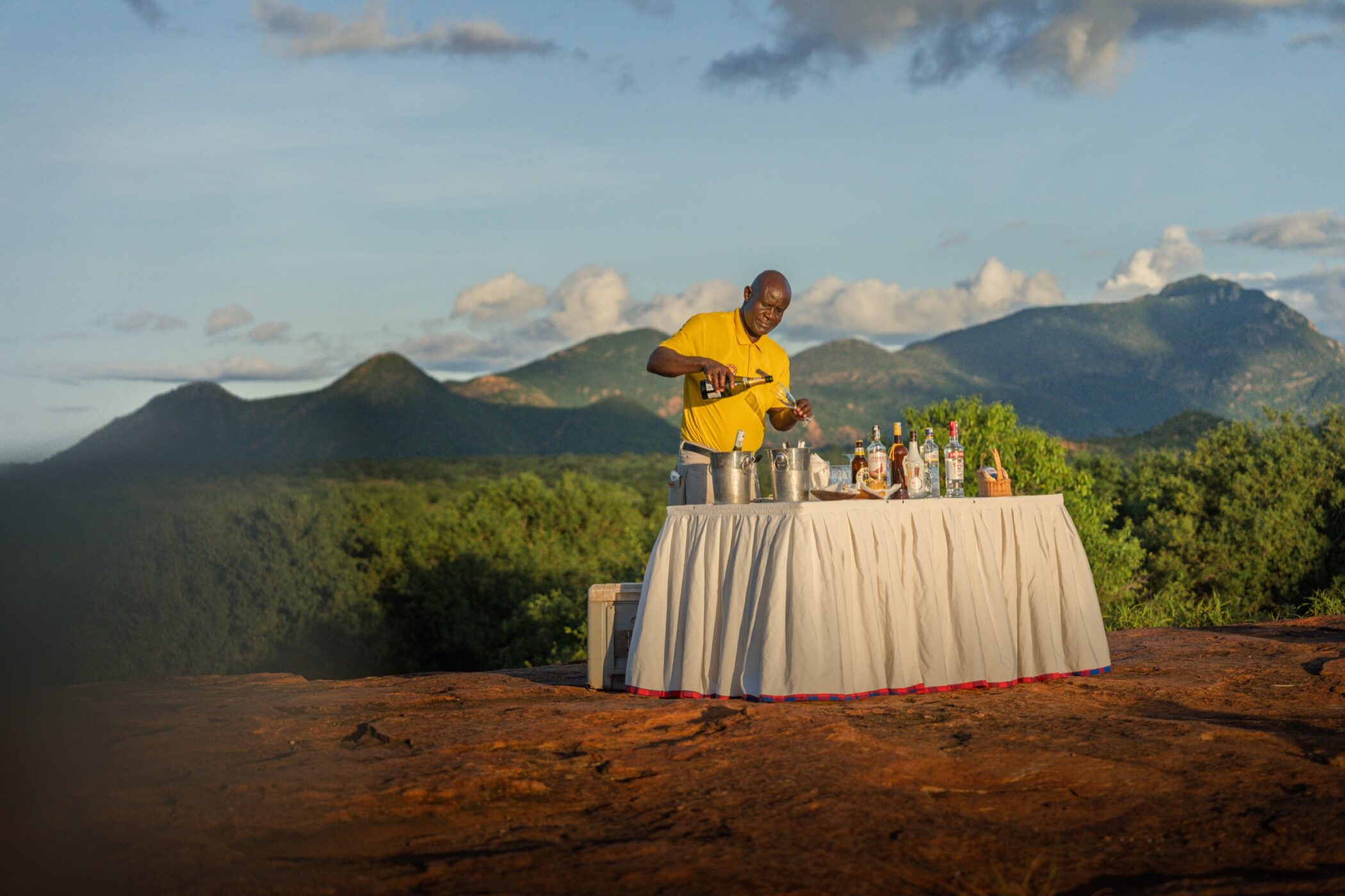 Guide preparing sundowner drinks above the Kenyan landscape