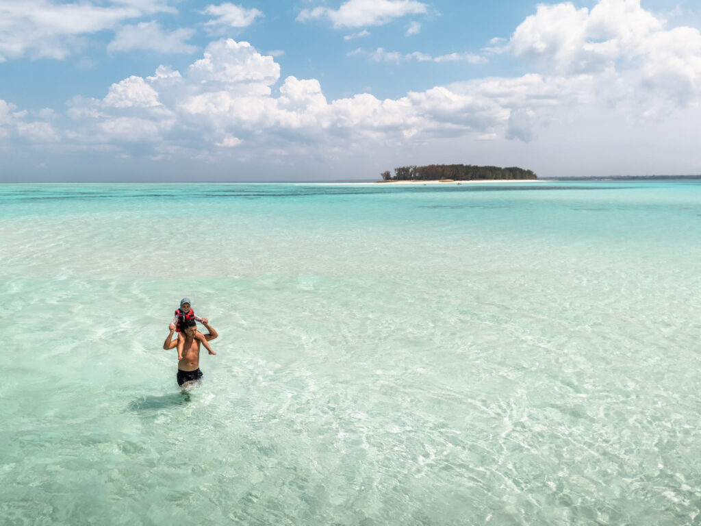 Father carrying a child through clear turquoise water during a Zanzibar catamaran excursion